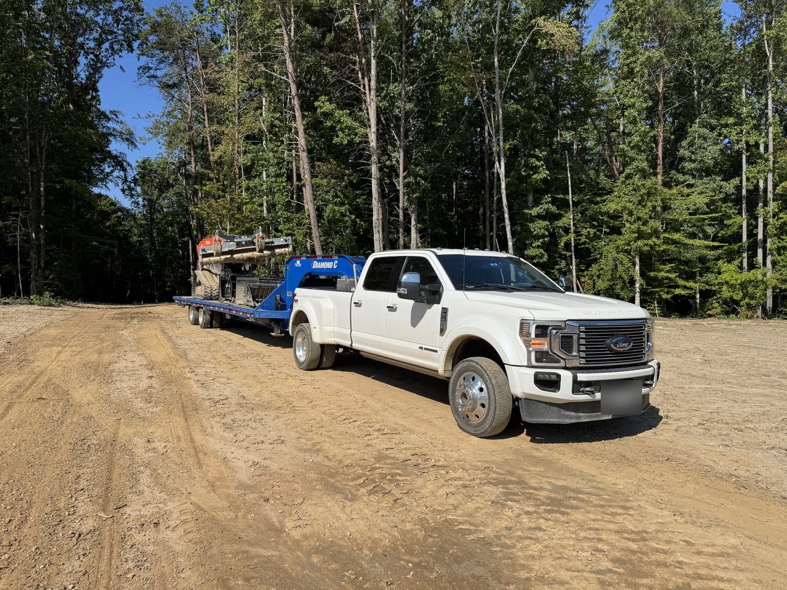 Home Free truck and gooseneck trailer carrying attachments on a freshly cleared lot